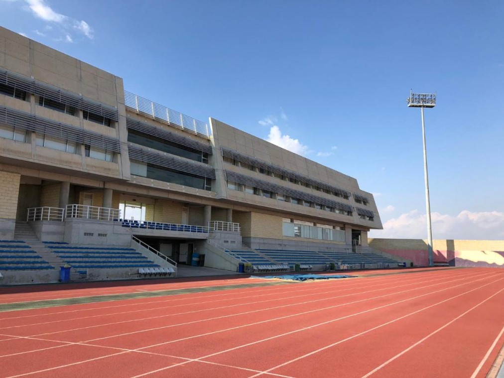 Athletics training facility with red track lanes and seating stands on a sunny day