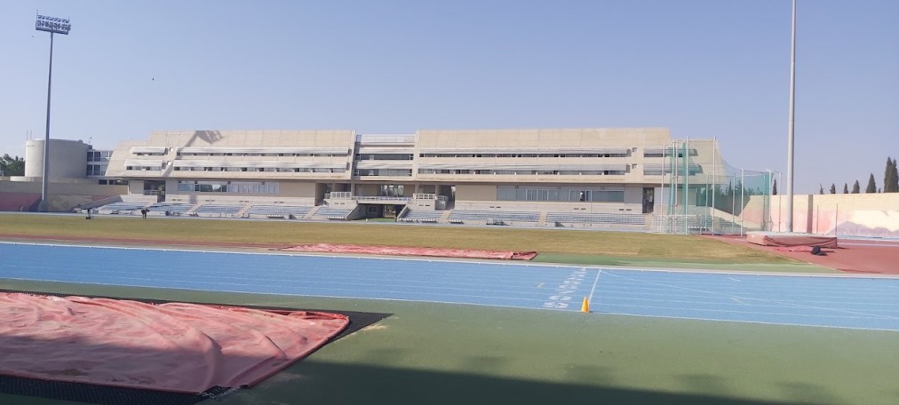 Wide view of sports complex featuring blue and red running tracks and central grass field