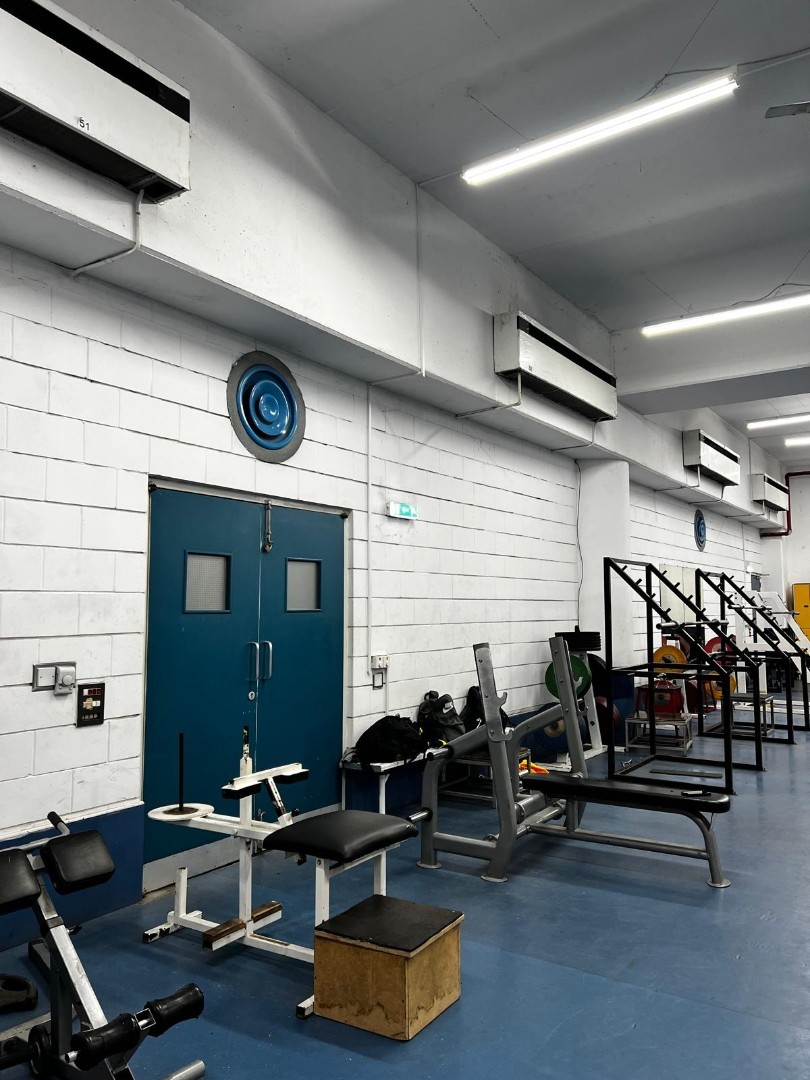 Indoor gym with weightlifting benches, racks, and blue flooring used for athlete strength training