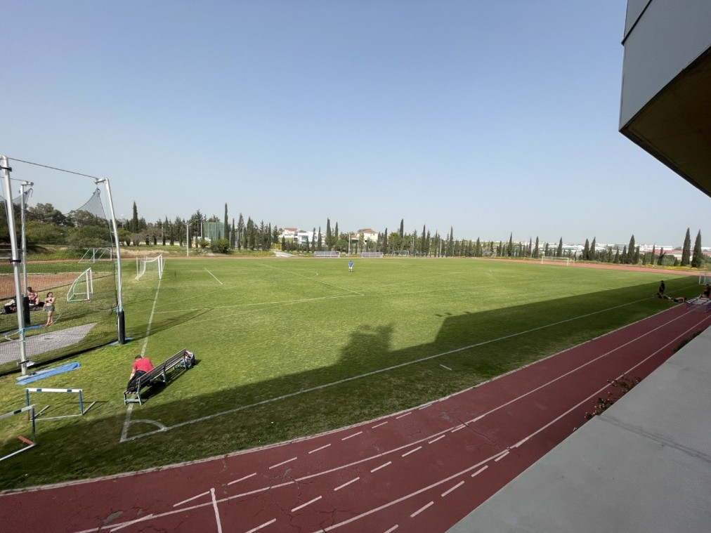 Wide view of grass football field with surrounding red running track and scattered athletes training
