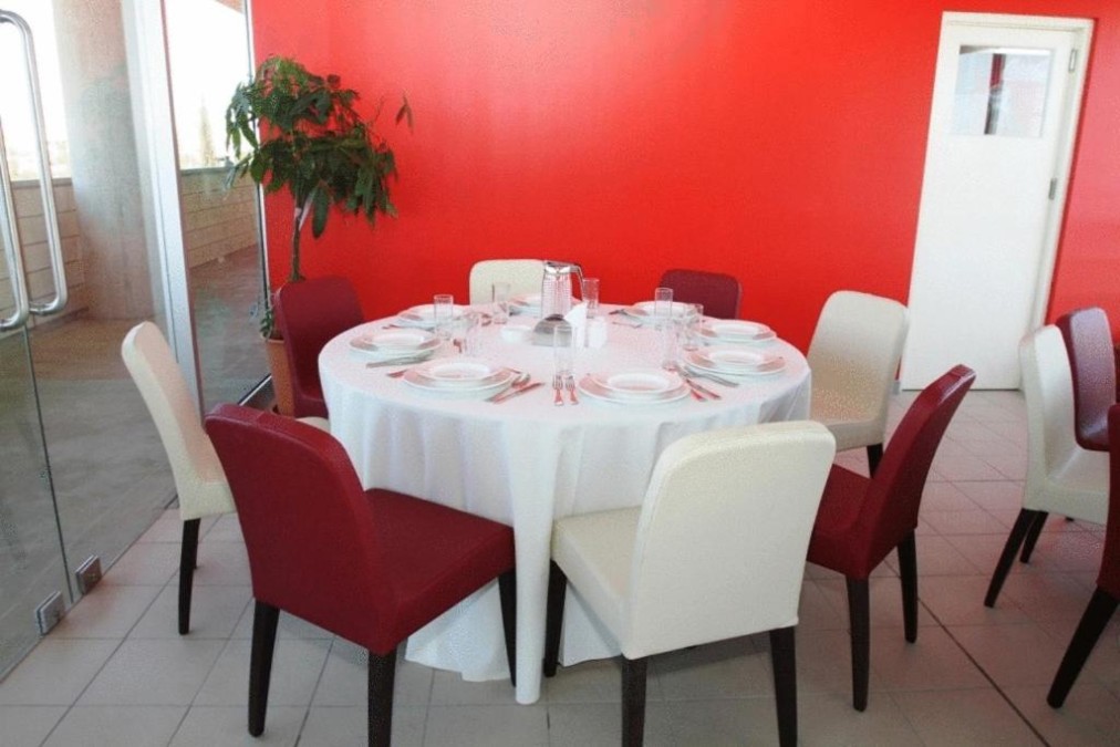 Round dining table set with white cloth, red and white chairs, and bright red wall backdrop