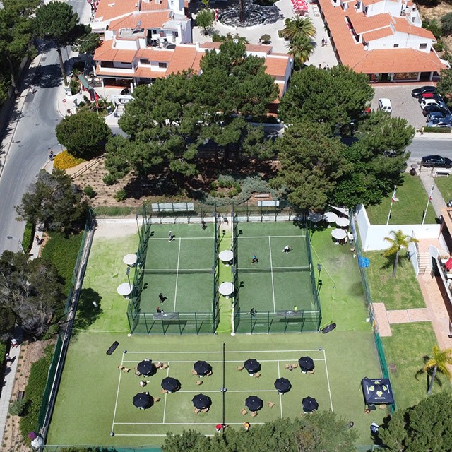 Aerial view of tennis courts with surrounding clubhouse and seating umbrellas.