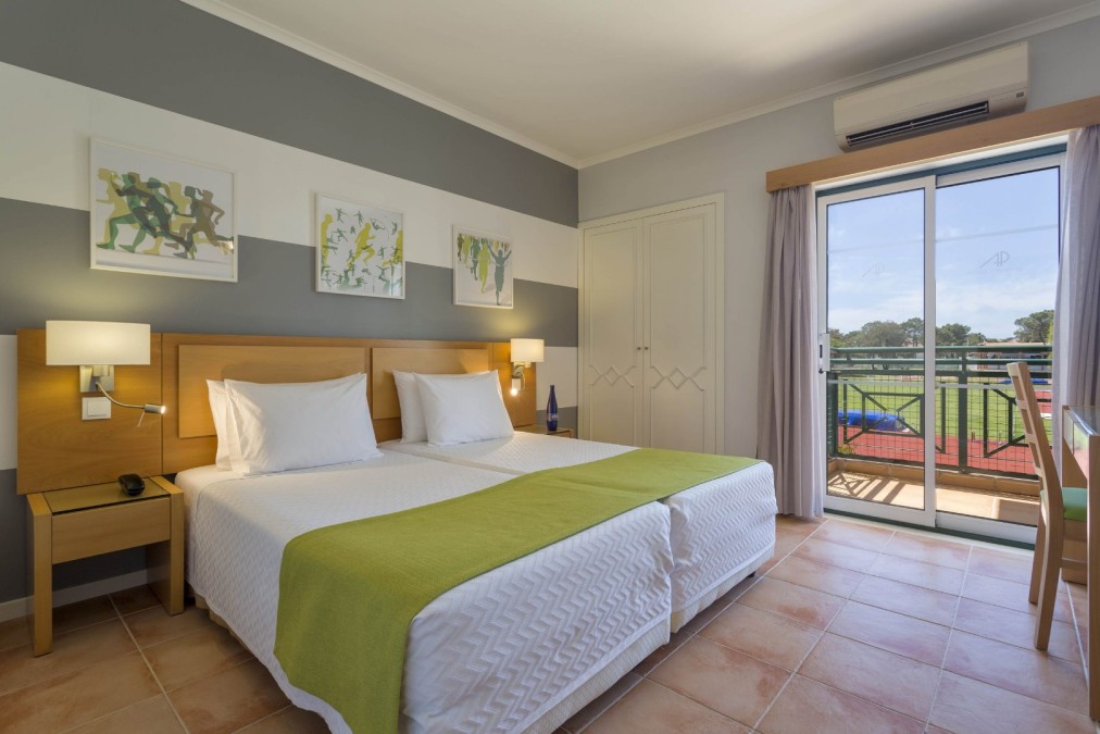 Twin-bed guest room with balcony and view toward the sports field.