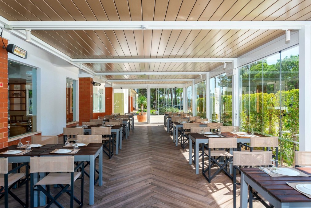 Covered outdoor dining terrace with set tables and glass walls.