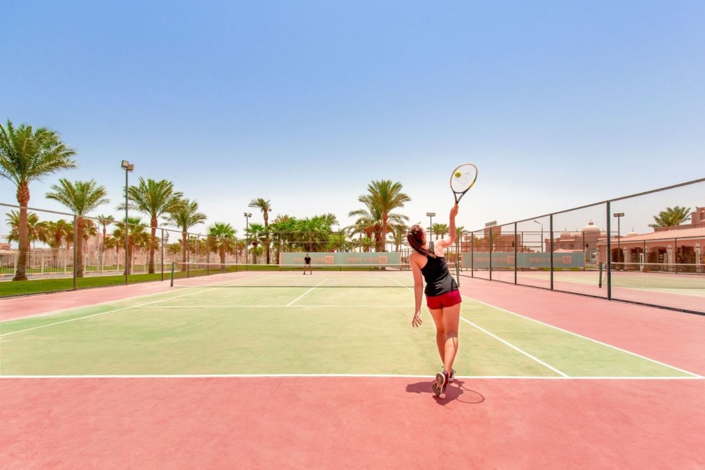 Female tennis player serving on outdoor court with palm trees