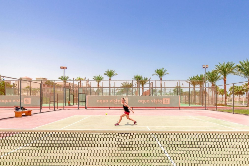Athlete playing tennis on red and green court under clear blue sky