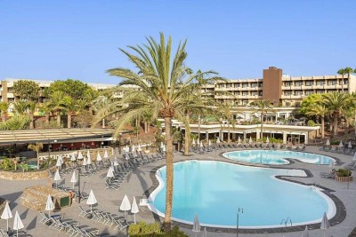 Curved outdoor leisure pool with sun loungers and palm trees in the resort grounds.