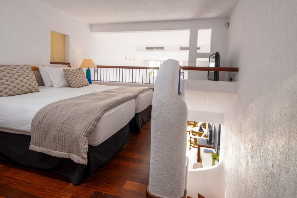 Loft-style hotel room with twin beds on an upper level and staircase below