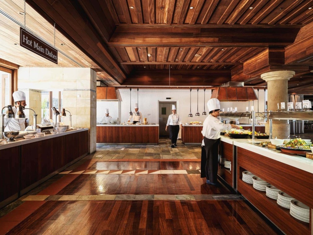 Chefs preparing food in a hotel buffet restaurant with wooden floors and serving stations