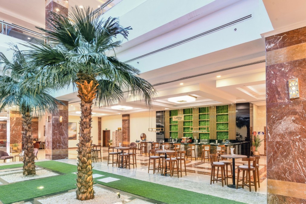Indoor bar area with palm trees, high tables and green shelves