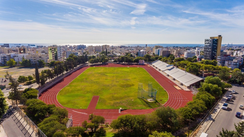 Wide view of athletics stadium with track, field, and bleachers near the sea