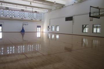 Empty indoor gym with a polished wooden court and a basketball hoop.