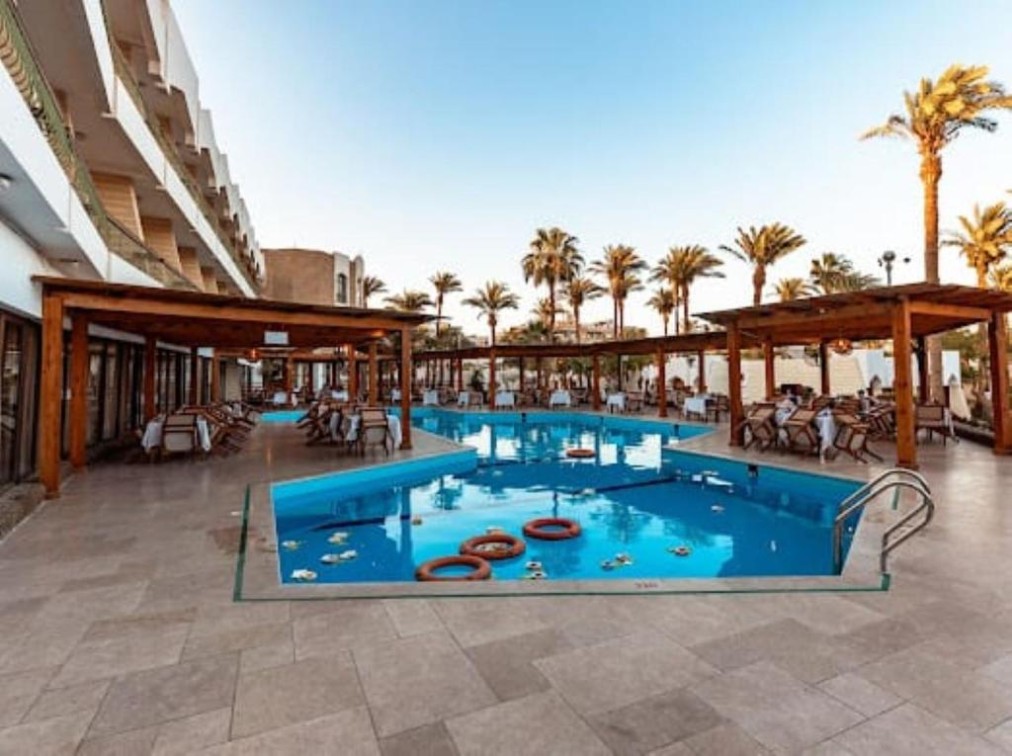Outdoor swimming pool with lounge seating under wooden pergolas.