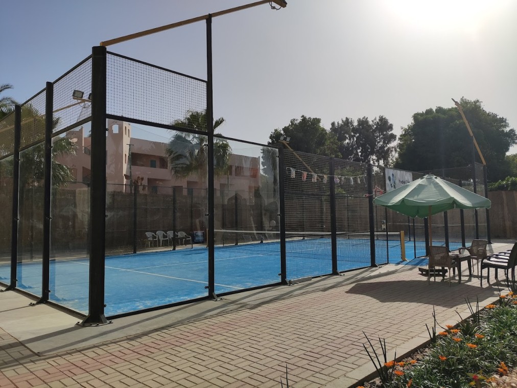 Outdoor padel court beside seating area with sun umbrella.