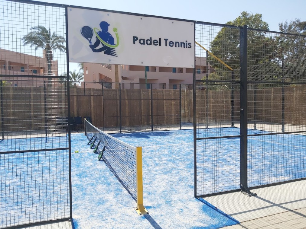 Padel tennis court entrance with net, fencing, and 'Padel Tennis' sign.