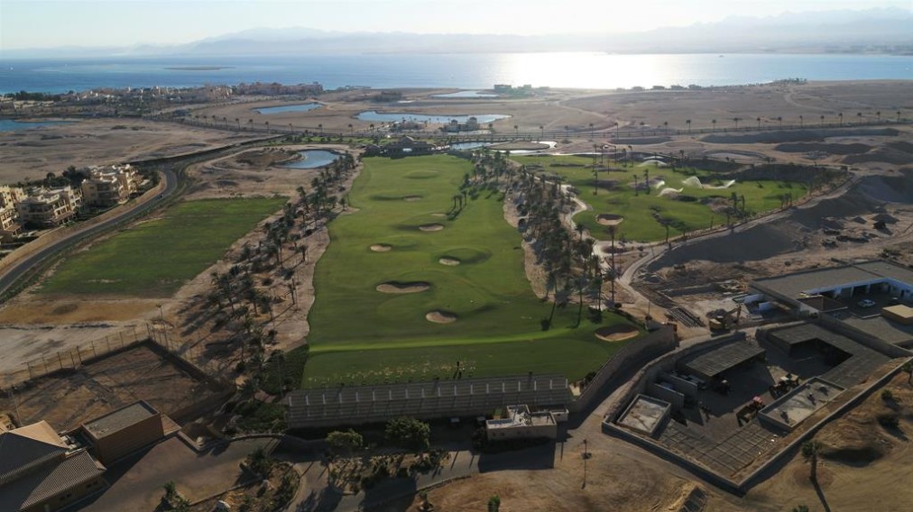 Drone view of a desert golf course with palm-lined fairways and bunkers near the coastline.
