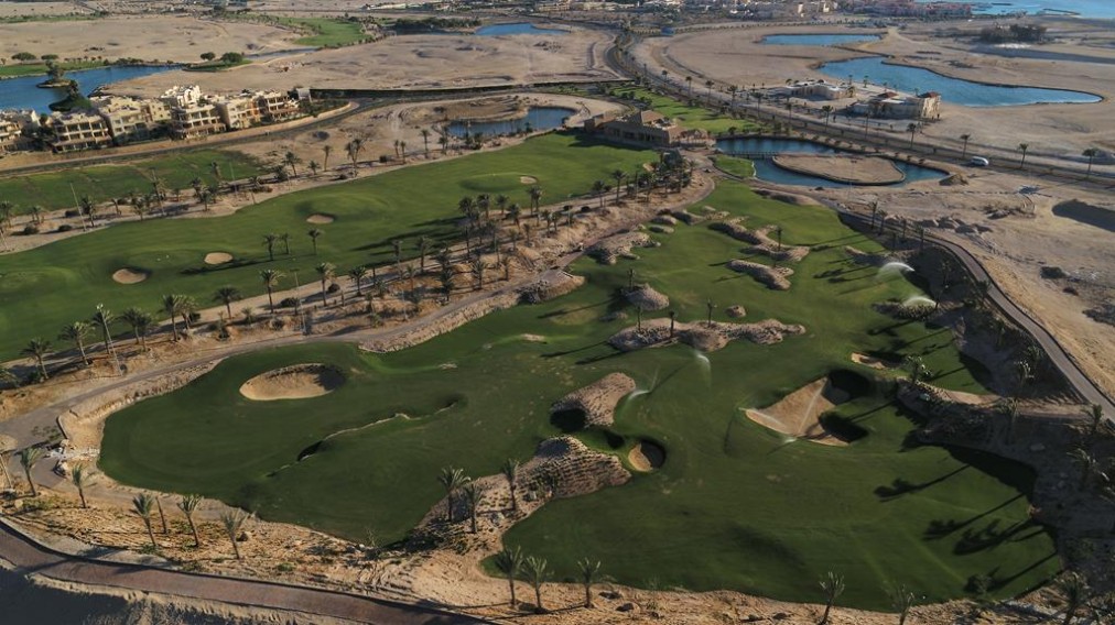 Aerial view of golf holes with bunkers and lagoons in a desert resort landscape.