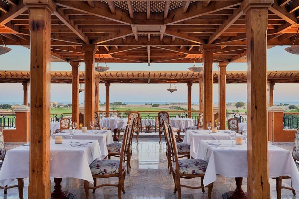 Covered terrace restaurant with set tables and views over golf course and sea