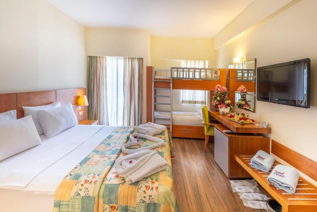 Hotel family room with double bed, bunk beds, desk, TV, and balcony curtains.