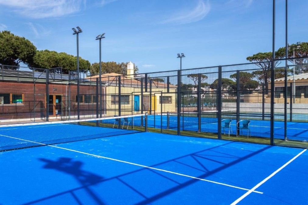 Blue padel court enclosed by glass and mesh fencing.