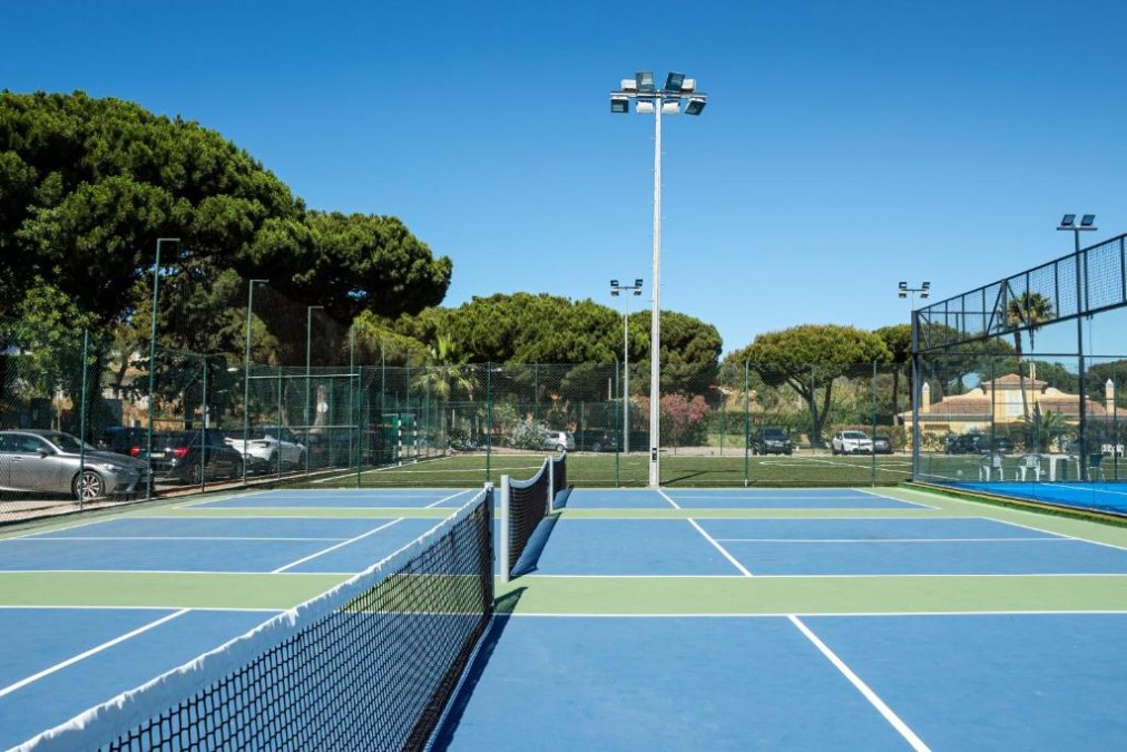 Outdoor tennis court with net, floodlights and perimeter fencing.