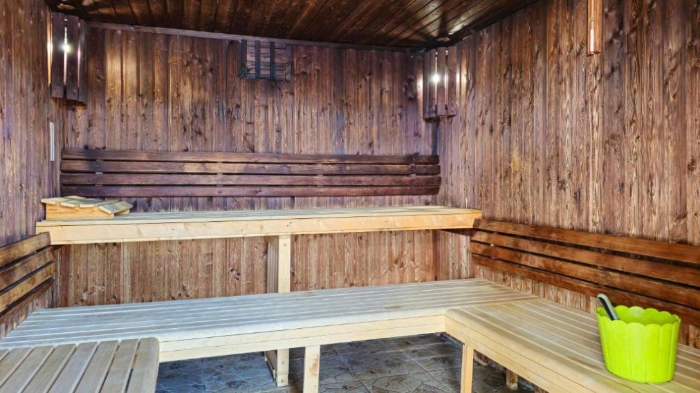 Wood sauna room with tiered benches and bucket.