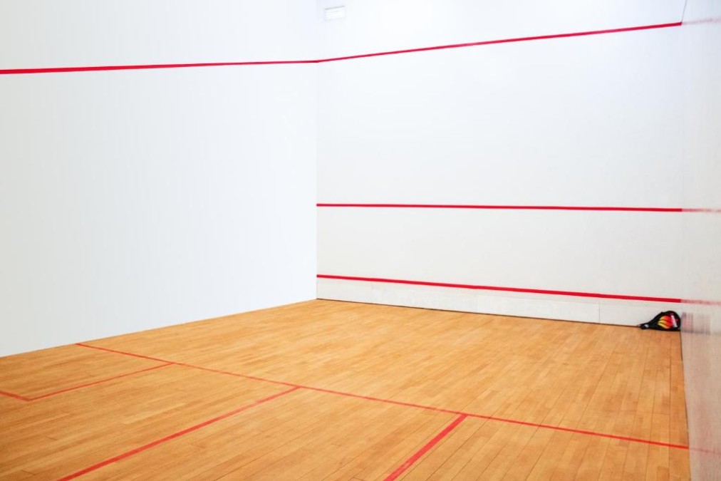 Indoor squash court with wooden floor and red boundary lines.