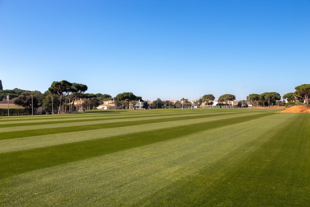 Wide grass training field with striped mowing patterns and sports posts.