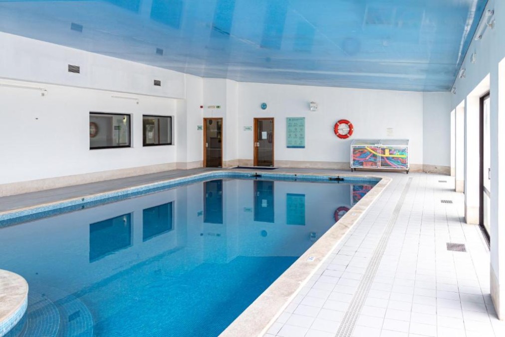 Indoor swimming pool with tiled deck and lifebuoy on the wall.