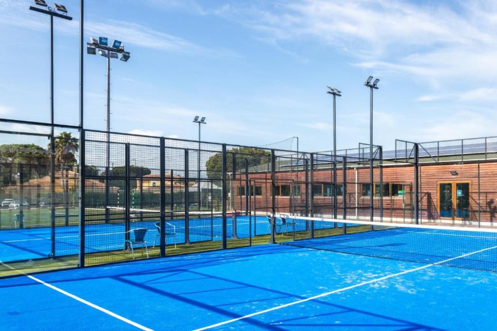 Padel court with floodlights and chairs beside the fenced playing area.