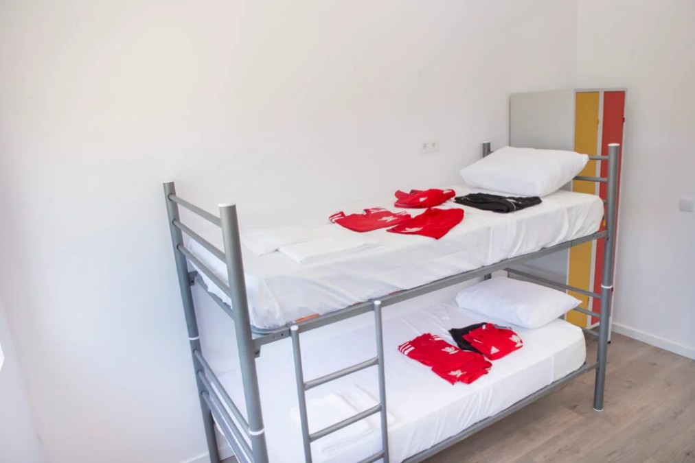 Bright bunk-bed room with white bedding and folded training camp sportswear.