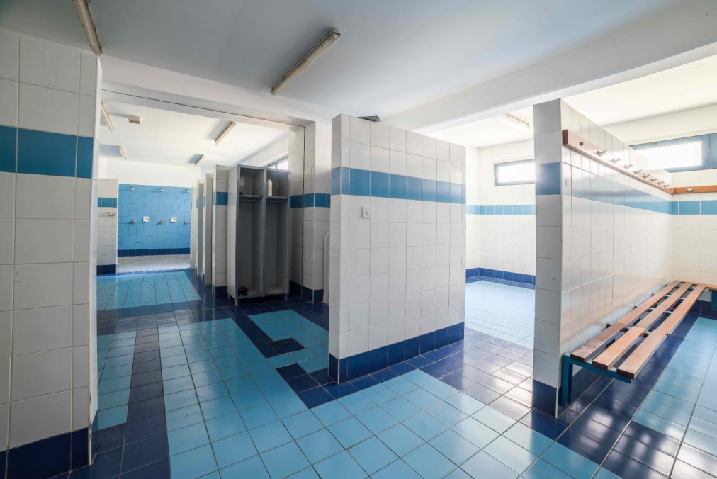 Blue-tiled locker room with benches, lockers and shower area.