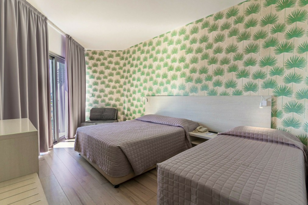 Hotel room with two double beds, green patterned wallpaper, and armchair