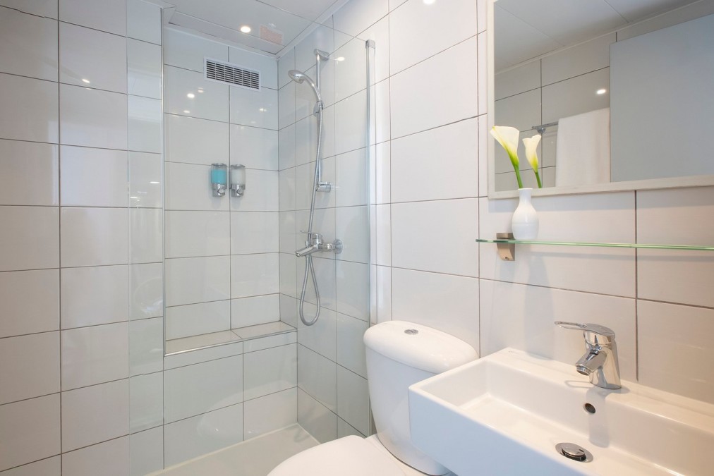 Clean tiled bathroom with shower, toilet, sink, and small decorative vase