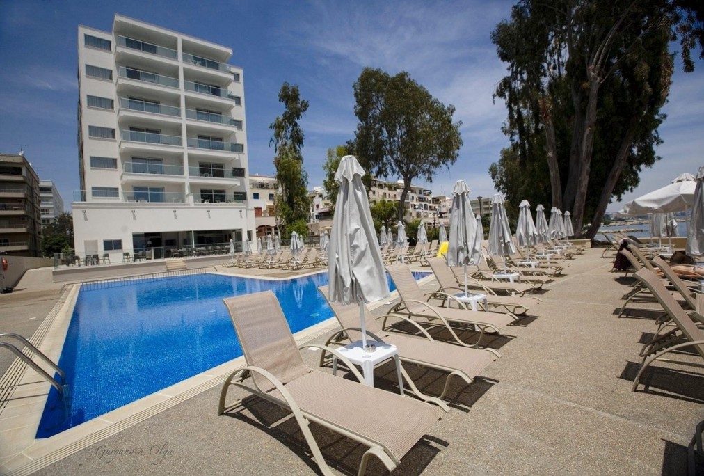 Outdoor pool area with sun loungers in front of a modern multi-story hotel