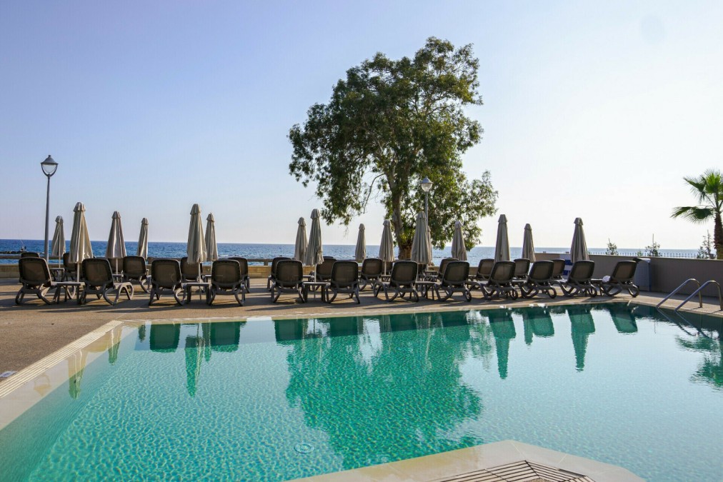 Outdoor pool with rows of sun loungers and umbrellas facing the sea