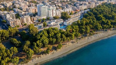 Aerial view of beachfront hotel complex surrounded by trees and city buildings near the coastline