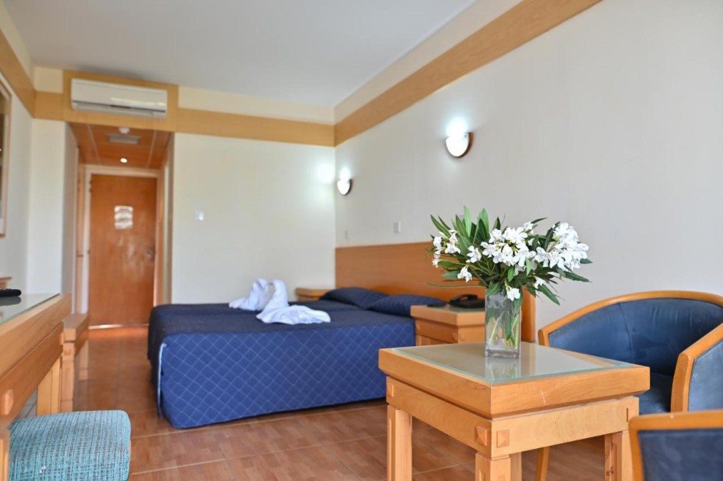 Guest room with double bed, seating area, desk and flower arrangement.