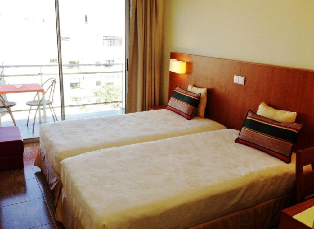 Twin room with balcony seating and daylight through sliding glass doors.