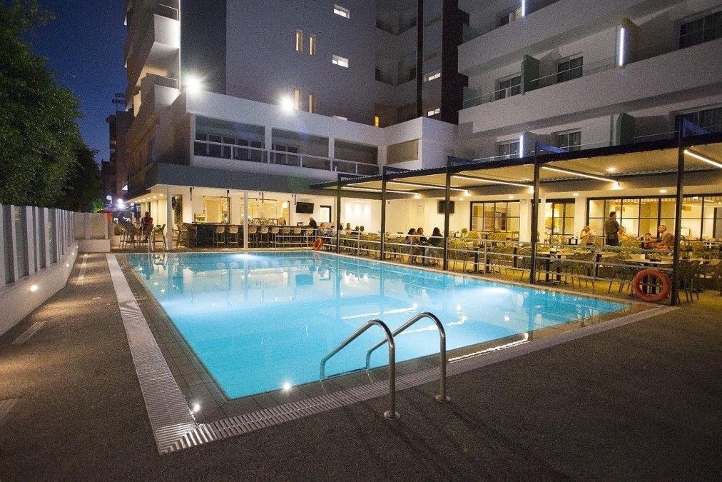 Outdoor pool at night beside the hotel terrace and bar seating area.