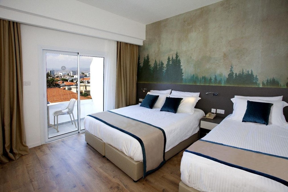 Room with one double bed, one single bed, a forest mural and balcony doors overlooking the city.