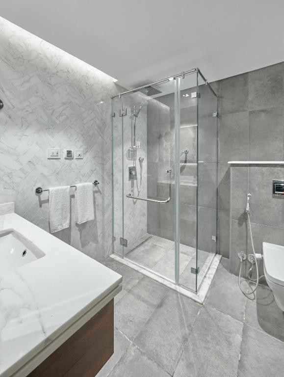 Modern bathroom with glass walk-in shower, gray tile, vanity counter, toilet, and white towels
