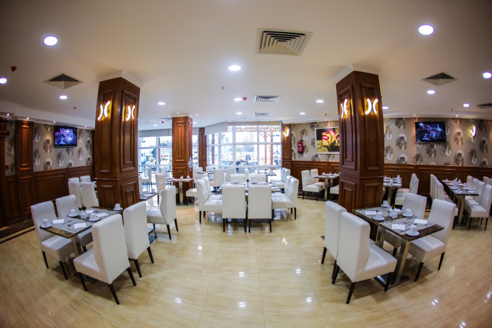 Restaurant dining room with set tables, white chairs, and wooden columns.