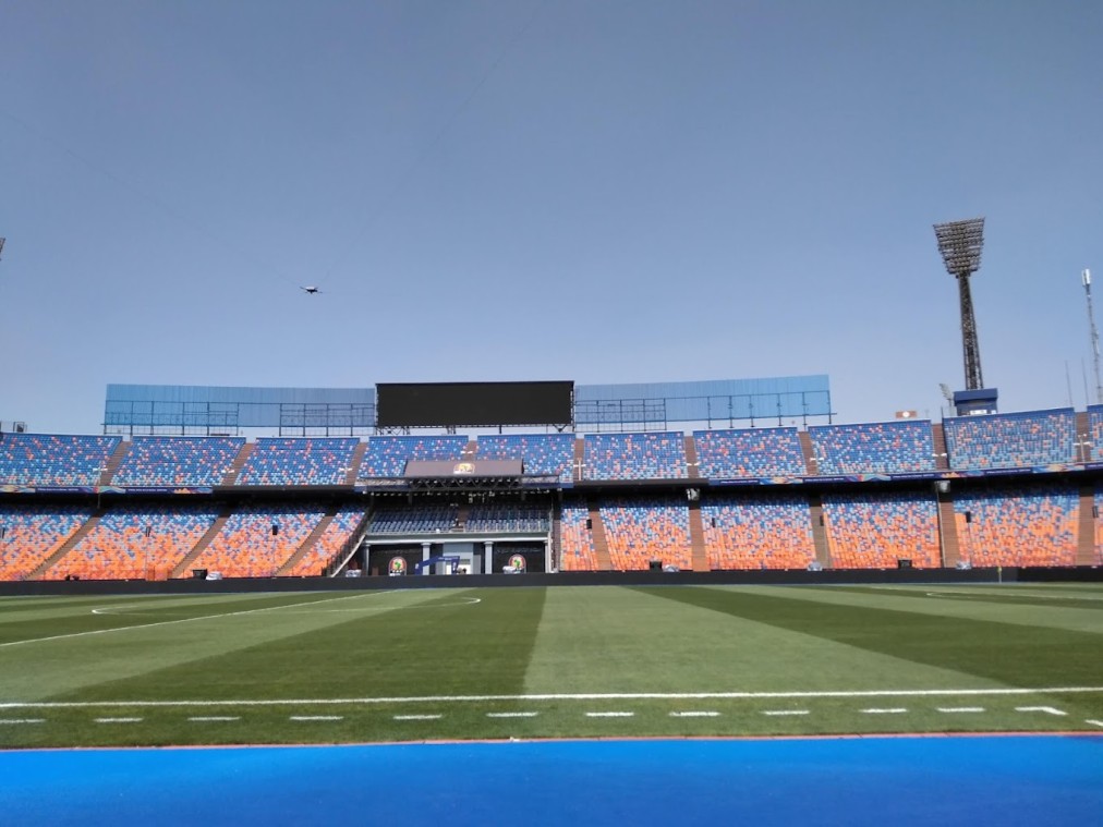 Empty football stadium with striped grass pitch, track edge, and a large video screen.