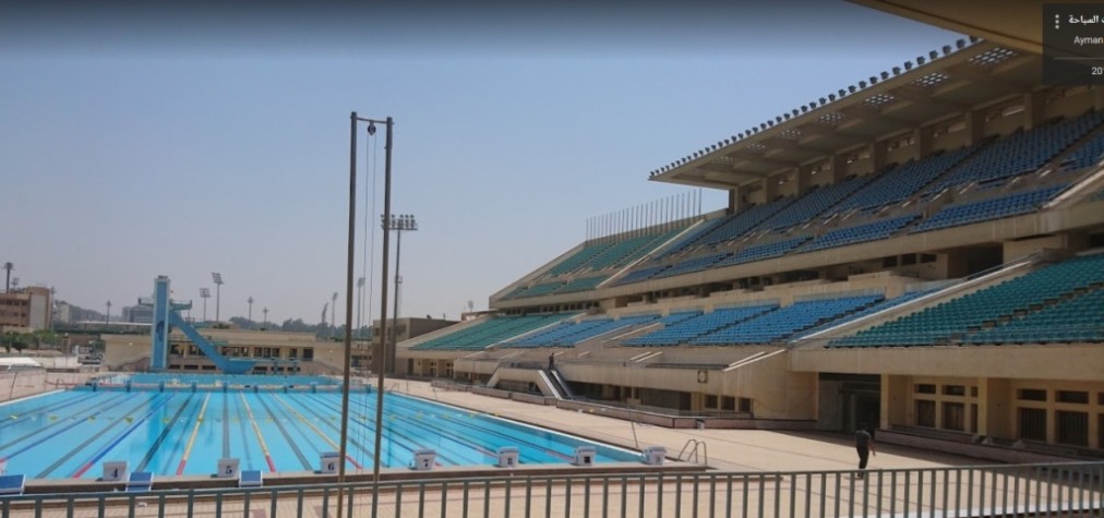 Outdoor 50m pool with starting blocks and large grandstand seating.