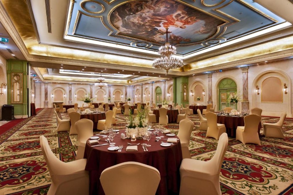 Large banquet hall with round dining tables, chandeliers, and an ornate ceiling mural.