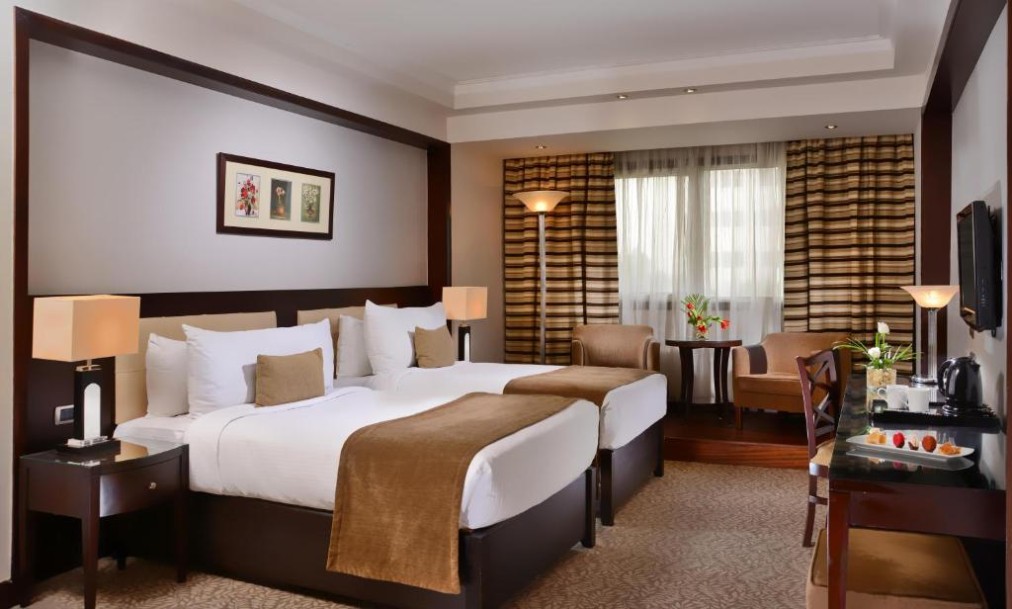 Twin room with two beds, seating corner, wall-mounted TV, and coffee/tea station.
