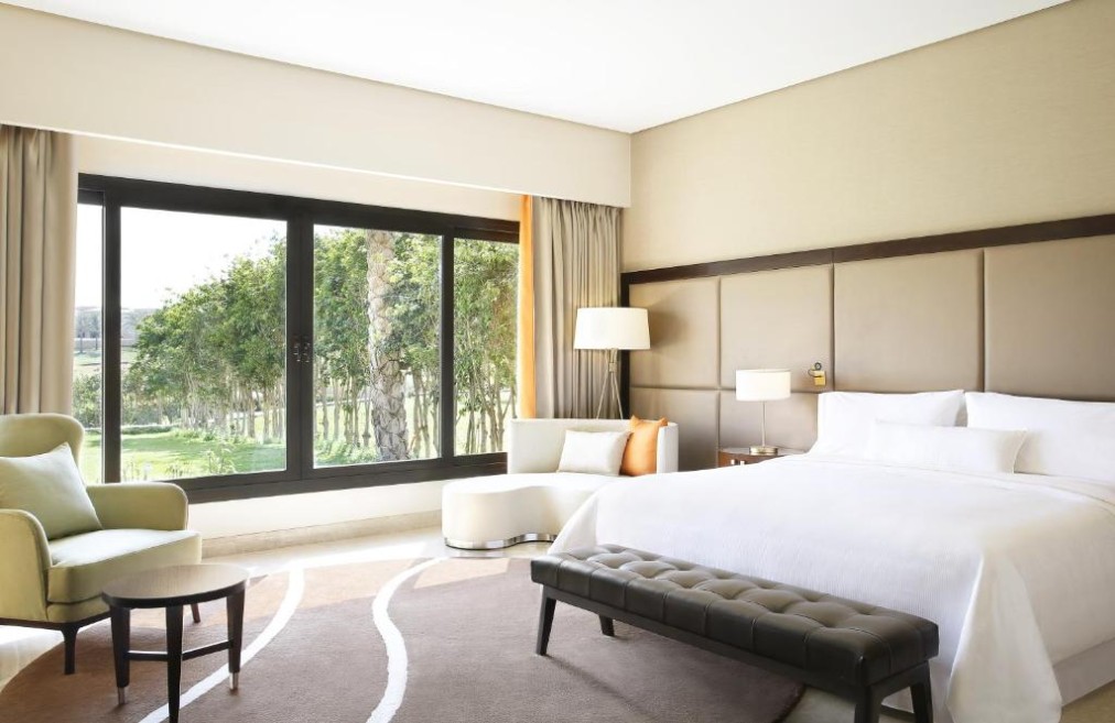Spacious king guest room with large picture window, lounge chair, and garden/green view.