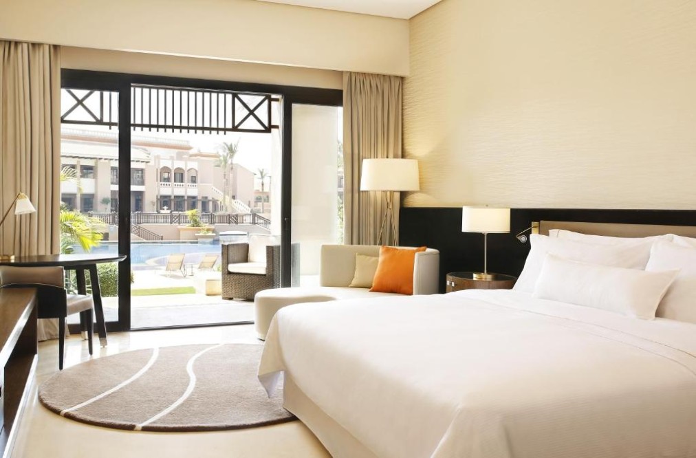 Bright king guest room with seating area and sliding doors opening to a terrace with pool view.