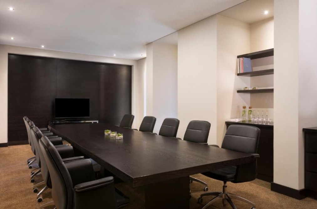 Boardroom-style meeting room with long table, leather chairs, and TV screen.